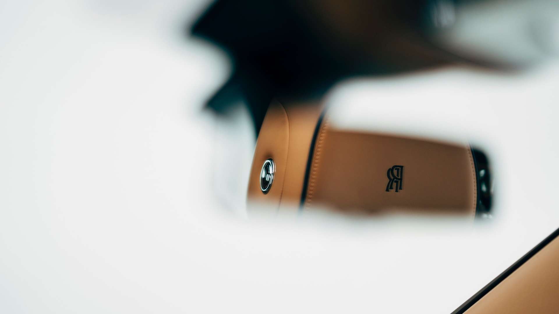 The logo of Rolls-Royce on a headrest of a Rolls-Royce Cullinan as seen in the reflection of the rear view mirror.