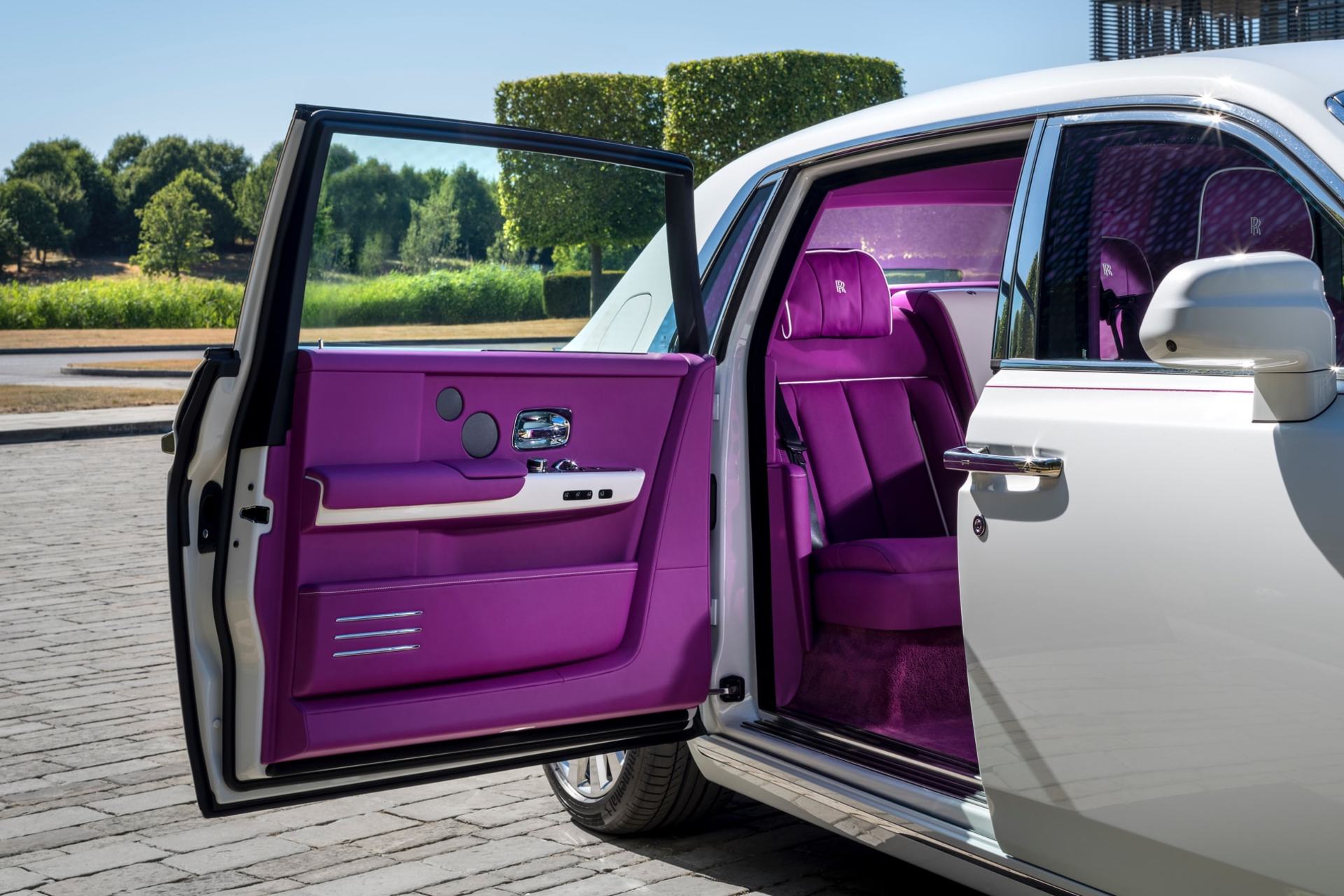 Exterior of a Rolls-Royce Phantom with its door opened, with a bright pink interior lining. 