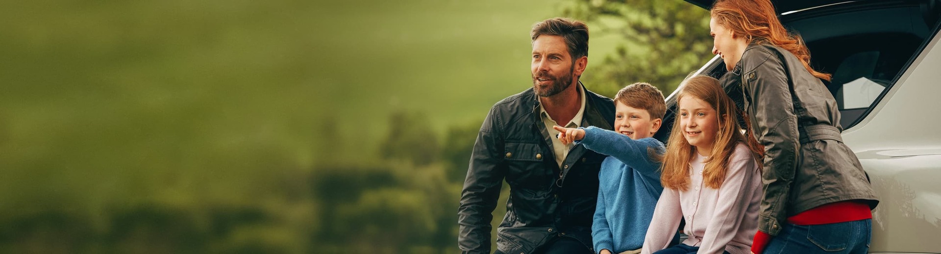Family beside Rolls-Royce Cullinan motor car looking to distance in countryside setting