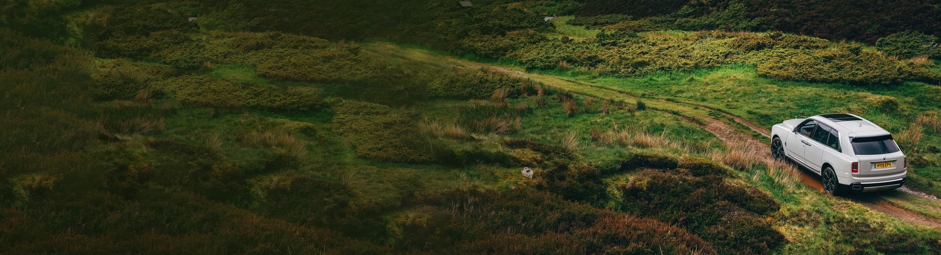 Aerial view of the Rolls-Royce Cullinan motor car traversing green countryside landscape 