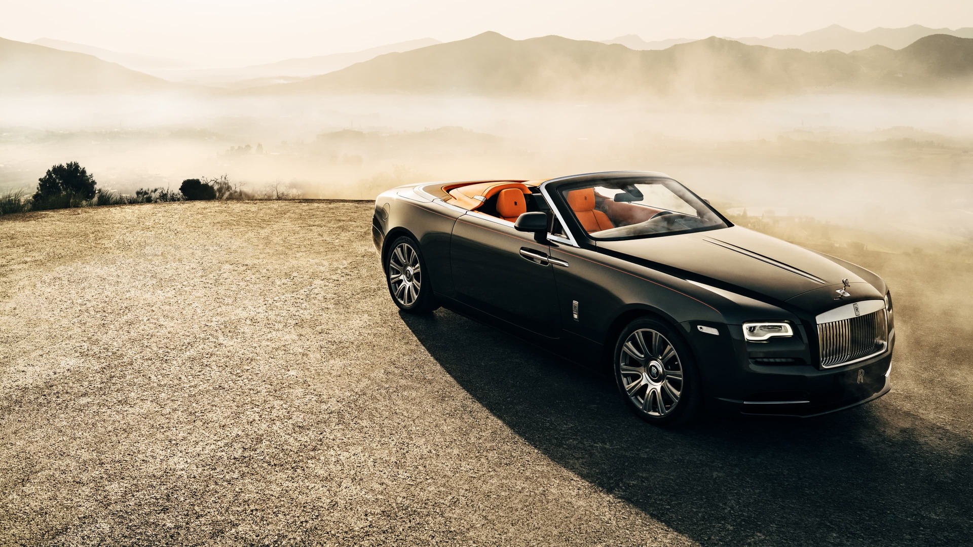 3/4 front exterior of stationary Rolls-Royce Dawn motor car with Dawn Aero Cowling Tonneau Cover open on sunny hilltop with expansive views