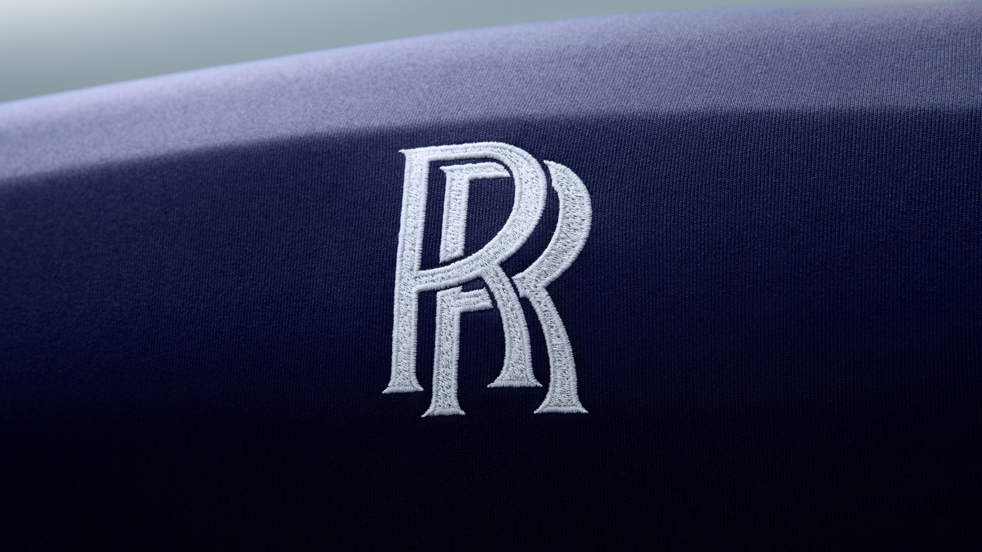 Detailed view of the embroidered RR monogram on the front of the Rolls-Royce car cover in navy blue colour