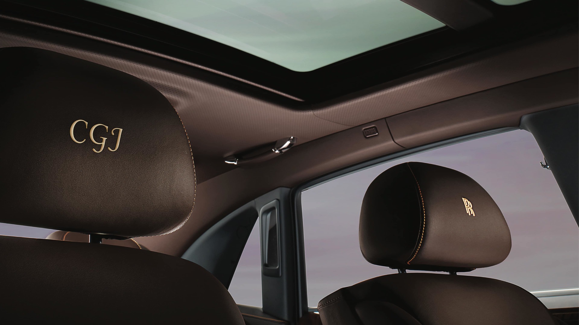 An interior shot of a Rolls-Royce Motorcar brown leather headrests, one embroidered with custom text and the other with the Rolls-Royce monogram