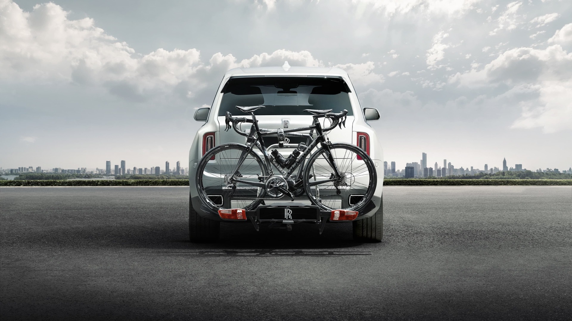 Rear exterior view of Rolls-Royce Cullinan motor car with tow bar mounted bicycle carrier with city in background