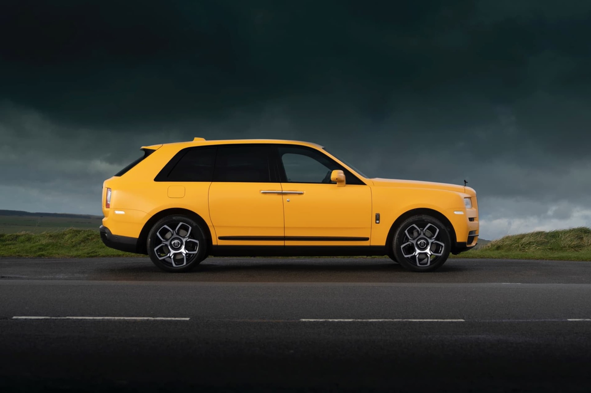 Side exterior view of the Rolls-Royce Black Badge Cullinan Capella motor car stationary with grey clouds above