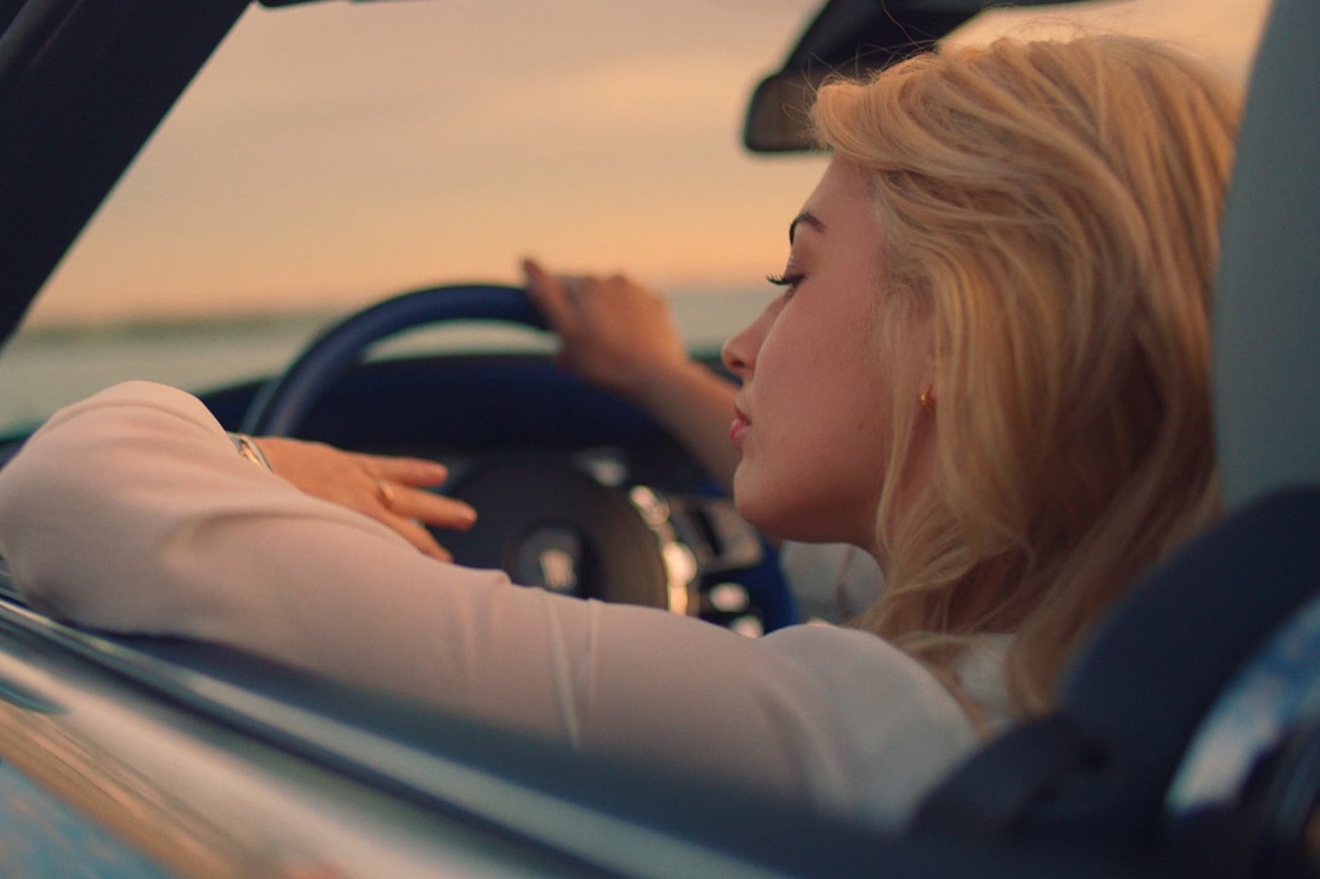 Woman drives drophead coupé Rolls-Royce Dawn motor car at sunset